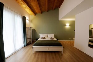 A bedroom with a wooden ceiling, a bed with a green blanket, a nightstand, and a wall-mounted mirror.