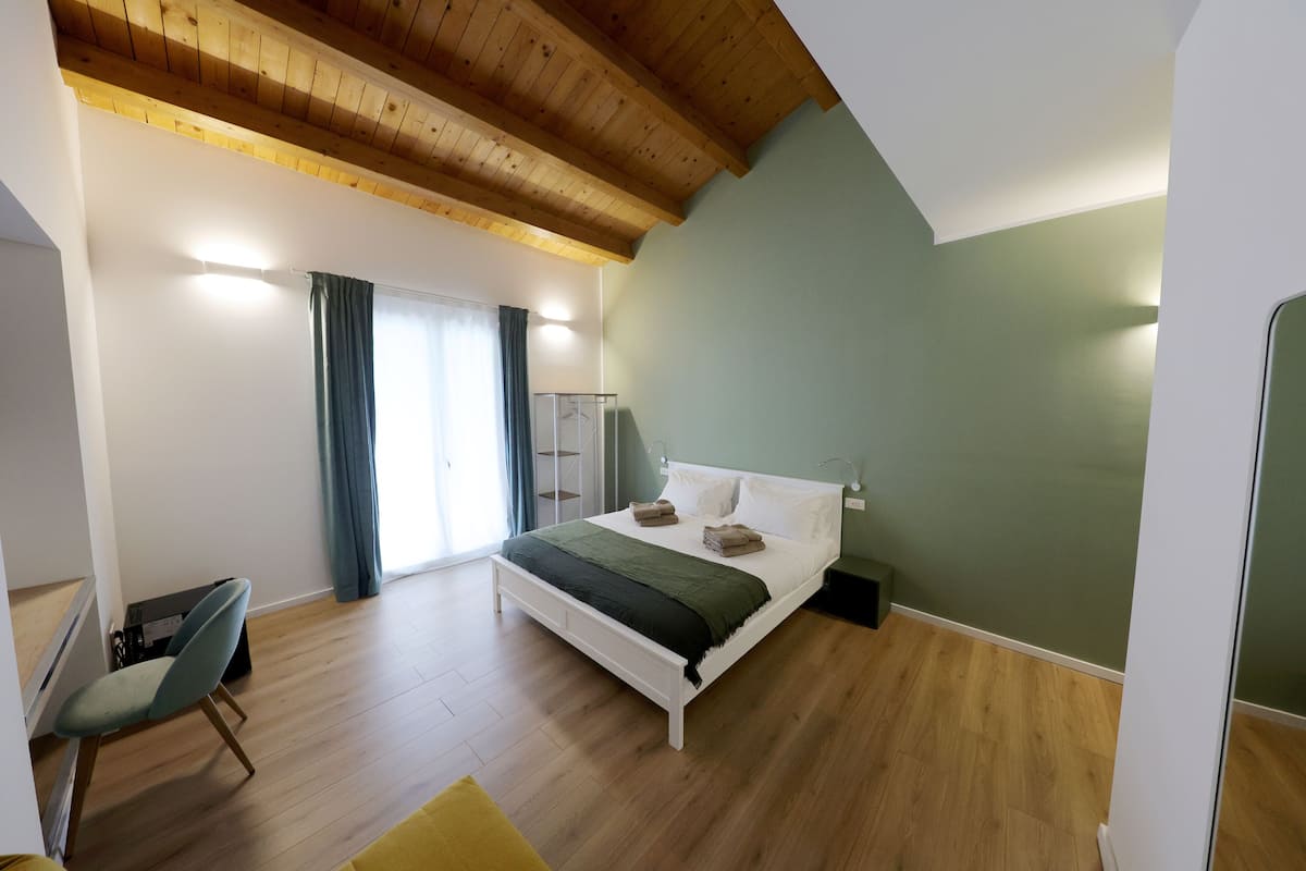 Une chambre avec un plafond en bois, un lit avec des oreillers et une couverture, une chaise et un bureau.