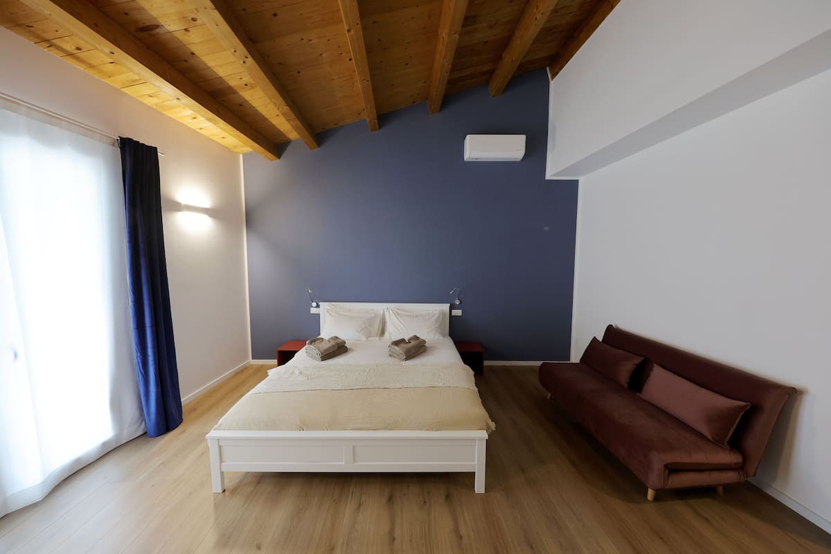 Une chambre avec un plafond en bois, un lit avec une literie blanche, un canapé marron et un mur bleu.