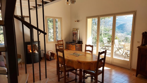 Un comedor con una mesa y sillas de madera, una chimenea y vistas al exterior a través de puertas correderas grandes.