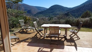 Un patio al aire libre con una mesa y sillas de madera, rodeado de una vista panorámica a las montañas.