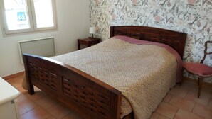 Un dormitorio con cama de madera, una silla, una mesita de noche y papel tapiz con motivos florales.