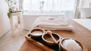 A bathroom with a bathtub, a wooden tray with bath salts, and a towel. - Hilltop Wellness Living (Ratsada)