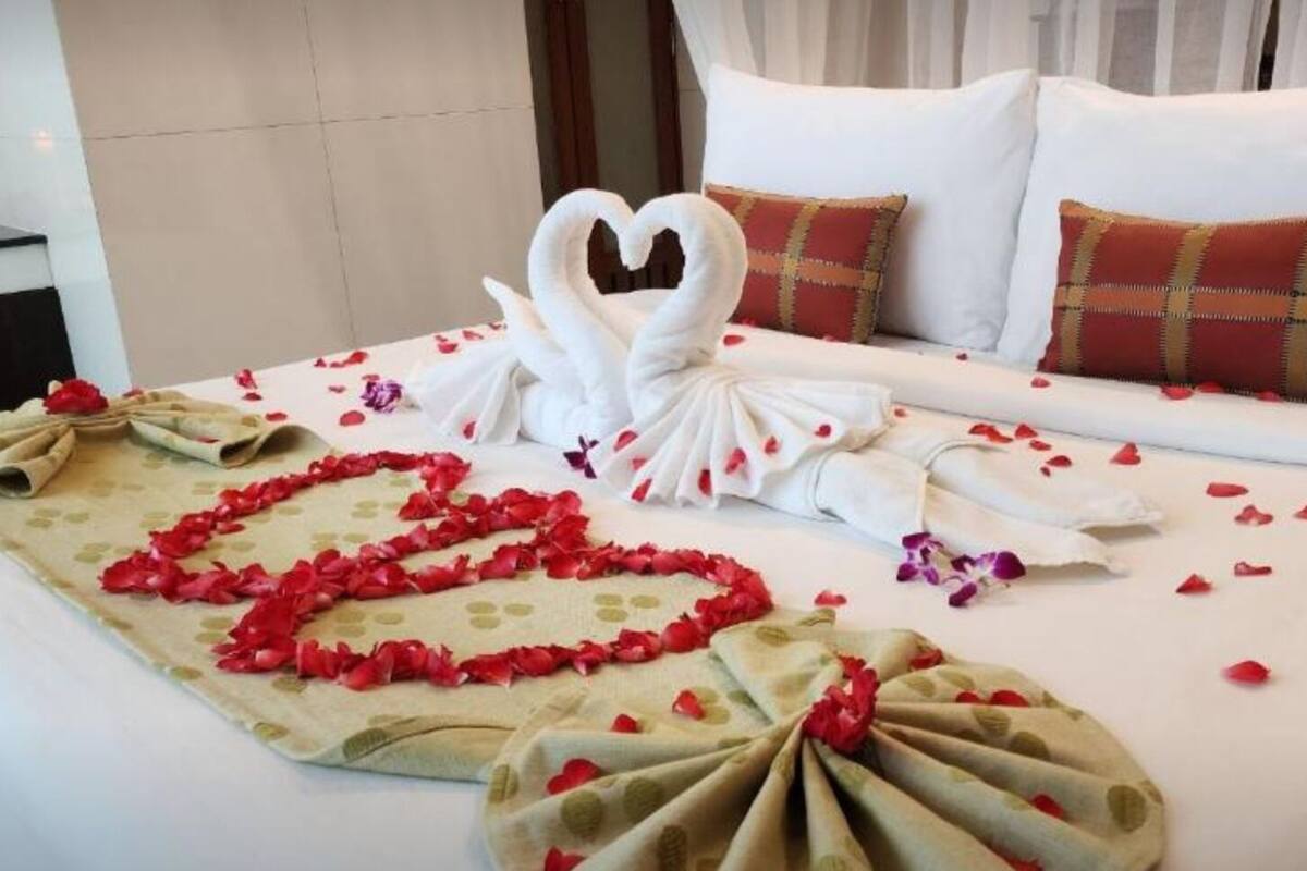 A neatly made bed with a heart-shaped arrangement of rose petals and a swan towel design.