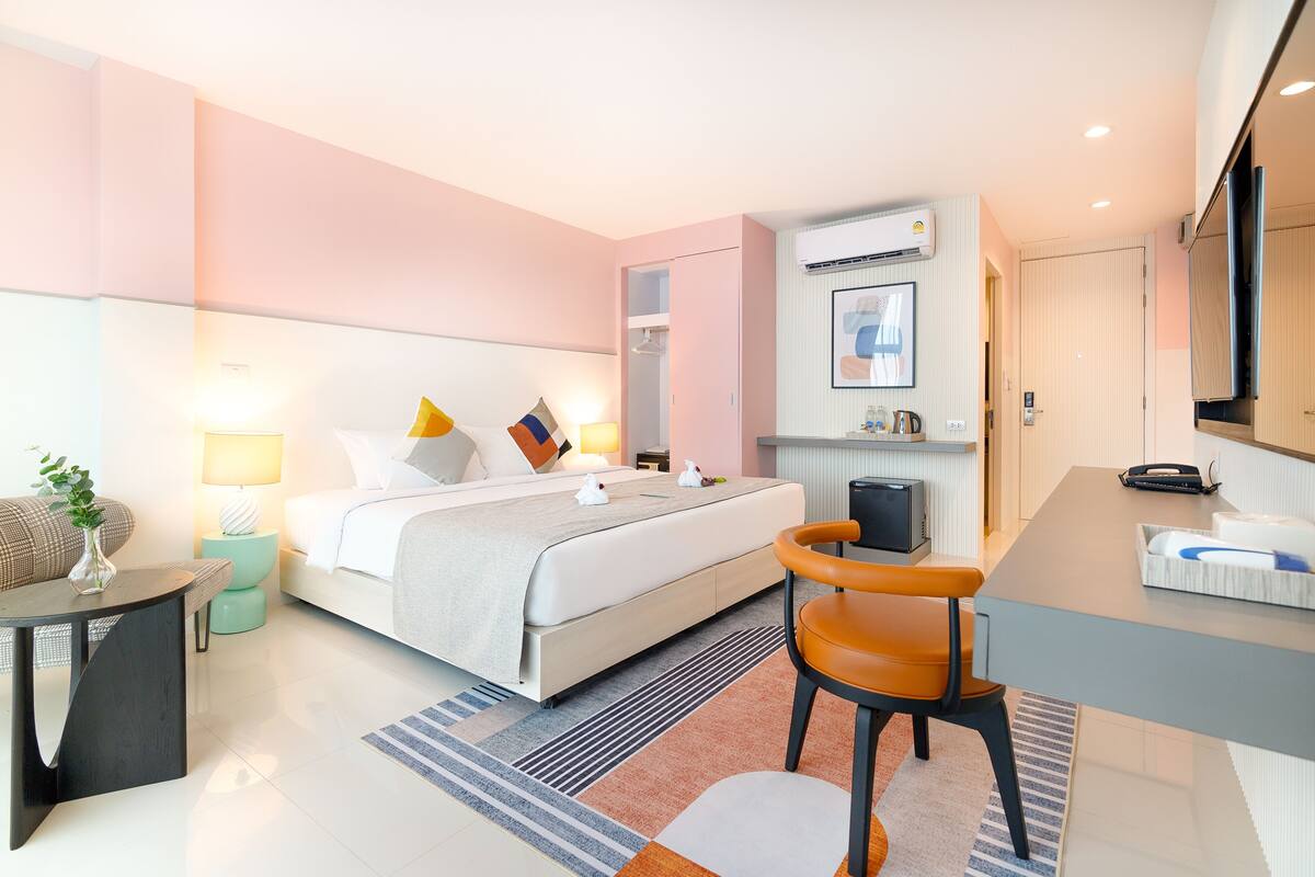 A modern hotel room with a bed, bedside table, chair, desk, and a television.