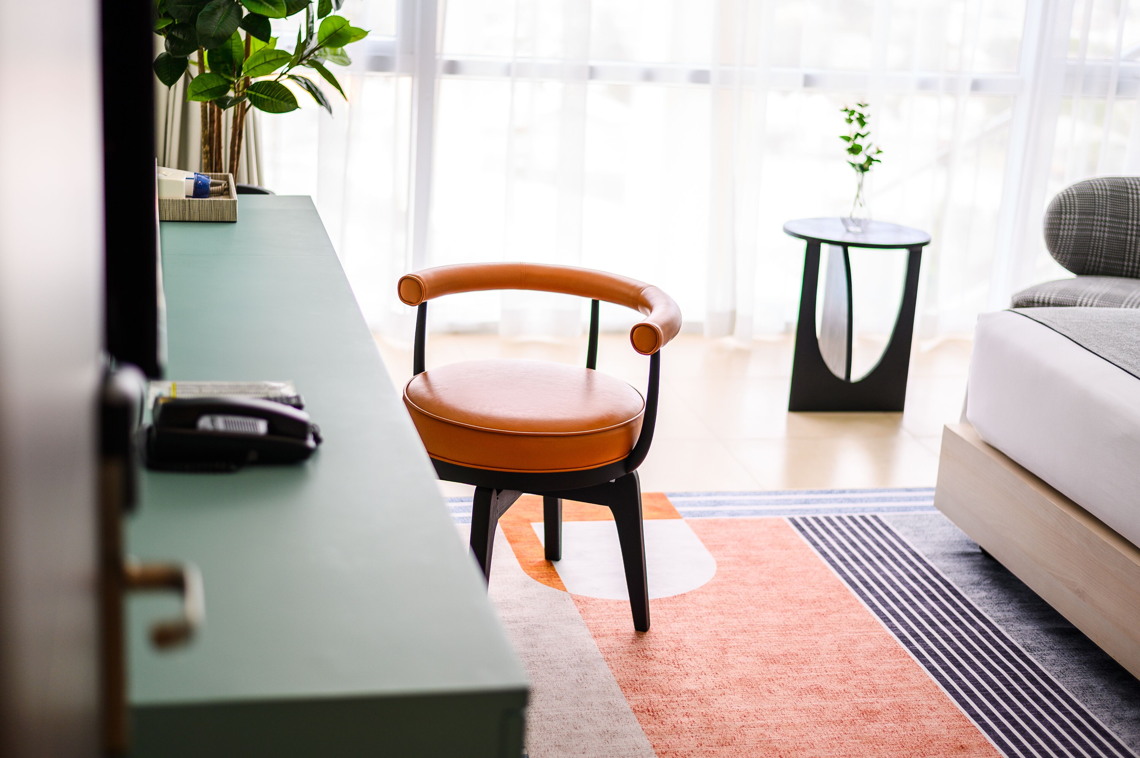 A modern living room with a green desk, a brown chair, a small round table with a plant, and a grey sofa.