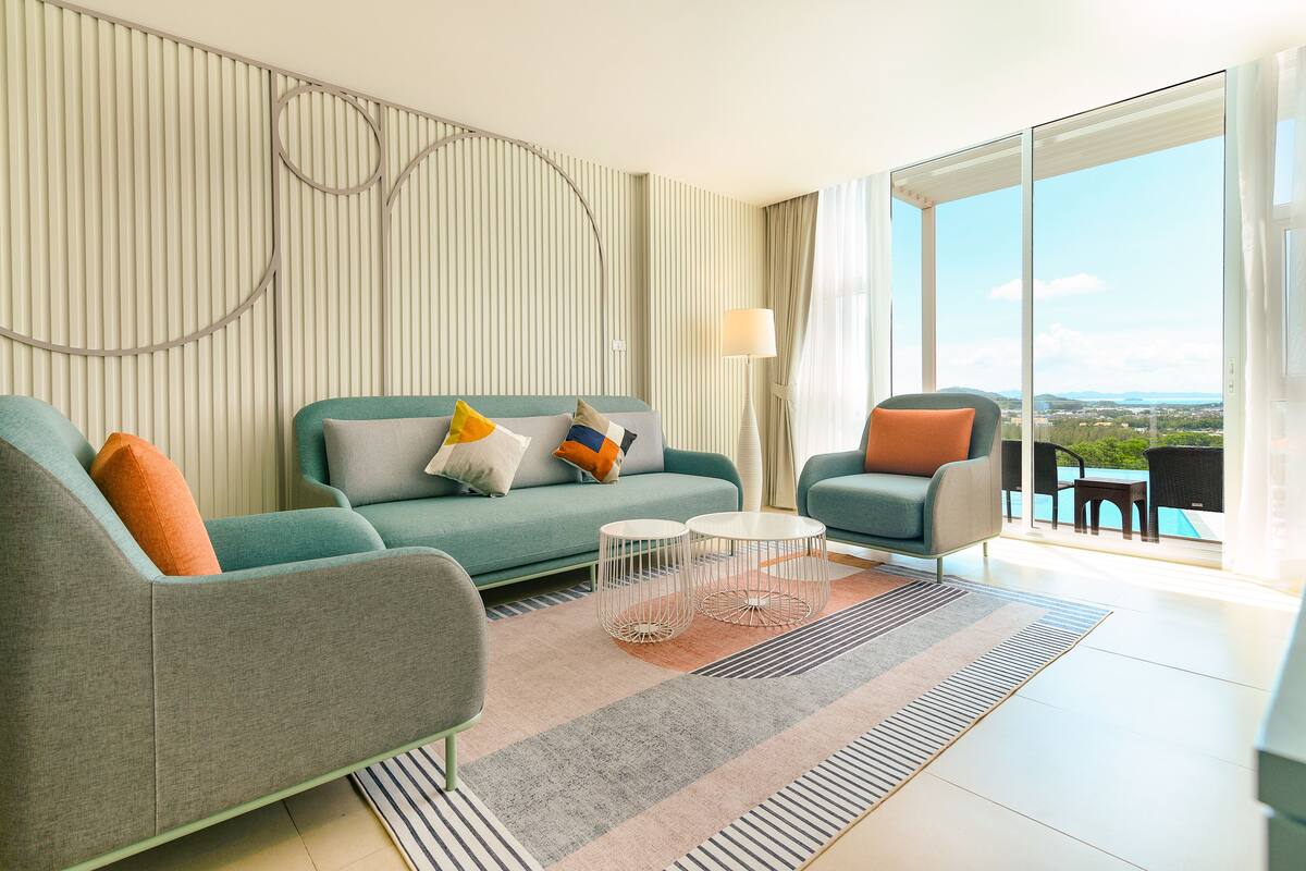 A modern living room with a sofa, armchairs, a coffee table, and a view of a pool and landscape.