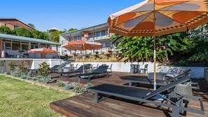Eine Terrasse mit Sitzgelegenheiten und Sonnenschirmen, umgeben von üppiger Vegetation und einem Gebäude mit Balkon.