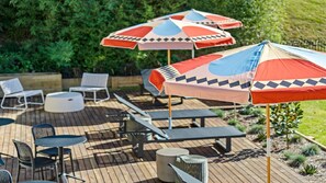 Eine Terrasse mit Sitzgelegenheiten, darunter Stühle und Tische, sowie mehrere farbenfrohe Sonnenschirme, die Schatten spenden.