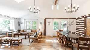 Un vaste salon doté d’une grande table à manger en bois, de nombreux espaces pour s’asseoir et d’un haut plafond avec des poutres apparentes.