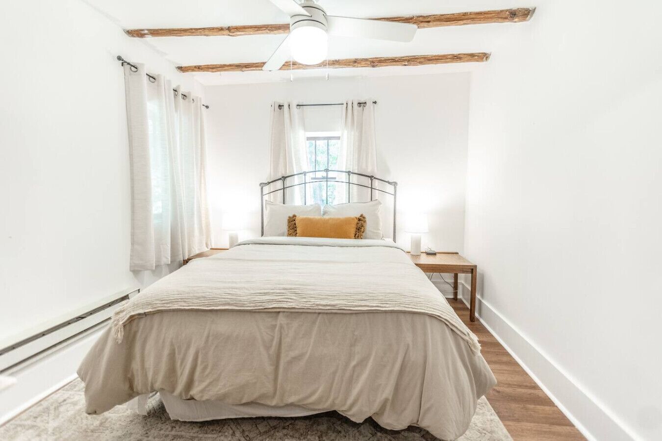 Ein Schlafzimmer mit einem Bett, einem Nachttisch, einem Deckenventilator und einem Fenster mit Vorhängen.