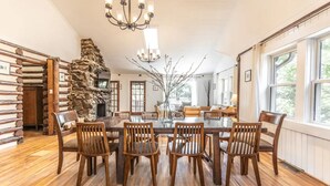 Une salle à manger avec une grande table en bois entourée de chaises, un mur en pierre et un lustre.
