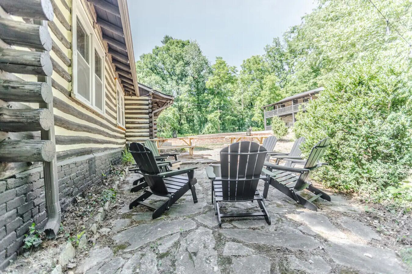 Une cabane en rondins avec un patio en pierre, deux fauteuils Adirondack et une terrasse en bois.