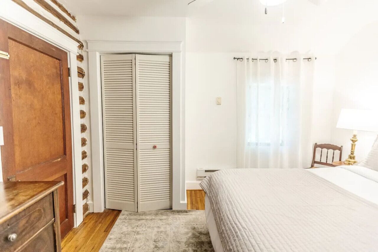 Un dormitorio con cama, armario de madera, armario con puertas empañadas, mesita de noche y lámpara.