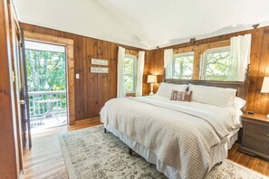 Un dormitorio con pared de paneles de madera, una cama con ropa de cama blanca, dos lámparas de noche y vistas a través de una ventana.