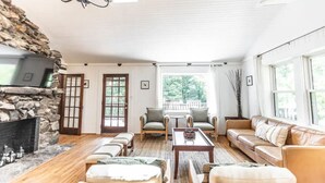 Una sala de estar acogedora con chimenea de piedra, piso de madera y un amplio ventanal con vistas al exterior.