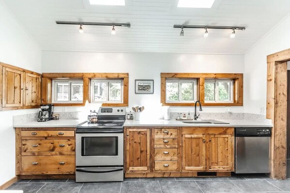 Una cocina moderna con armarios de madera, horno empotrado, lavavajillas y ventanas amplias.