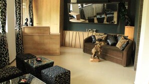 Ein Wohnzimmer mit einer Couch, zwei Sesseln, einem Couchtisch und einem Beistelltisch. An der Wand befindet sich ein großer Spiegel und ein Holzschrank.