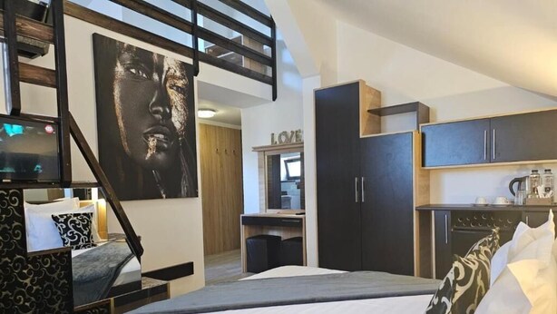 Ein modernes Hotelzimmer mit Bett, Schreibtisch, Kleiderschrank und Küchenzeile.