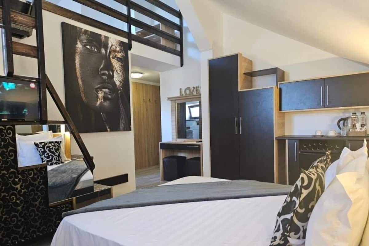 A modern hotel room with a bed, a desk, a wardrobe, and a kitchenette.