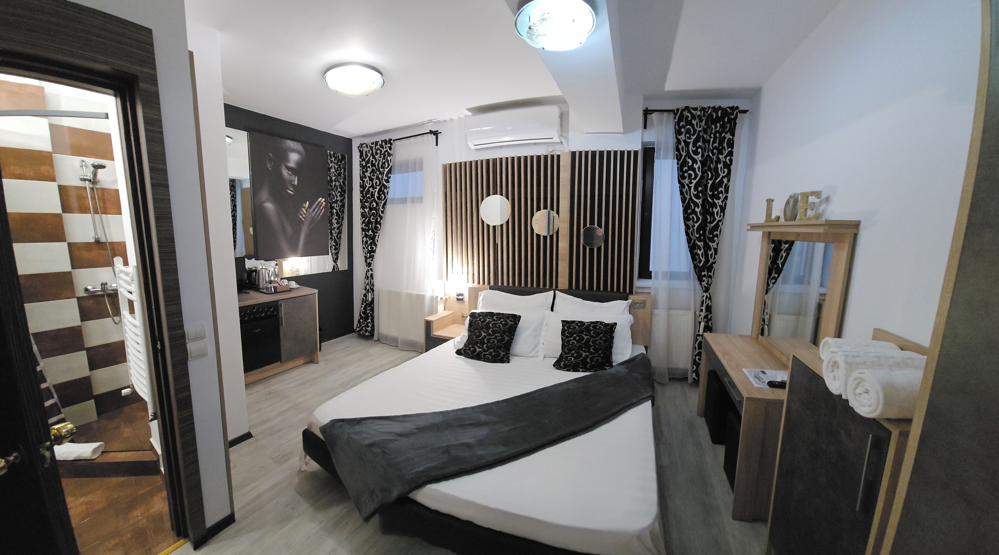 Et moderne hotelværelse med seng, natbord, spejl og udsigt til badeværelset.