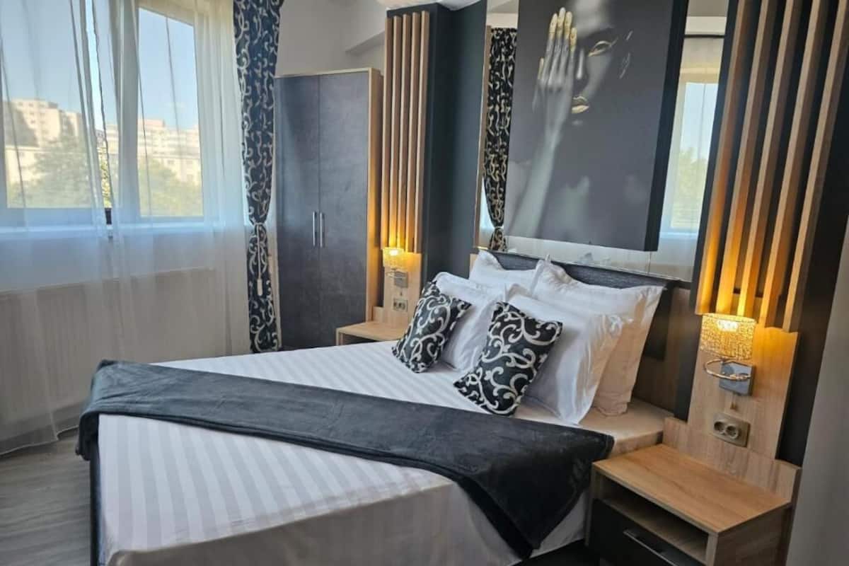 A modern bedroom with a large bed, bedside tables, a mirror, and curtains.
