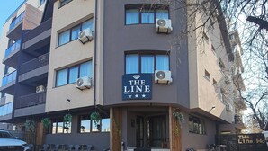 Ein Gebäude mit der Beschilderung 'THE LINE', Klimaanlagen, einem verschlossenen Eingang, Außenbestuhlung und einem geparkten Auto.