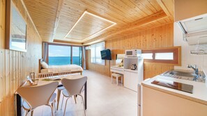 A wooden cabin with a bed, a desk, a TV, and a kitchen area.