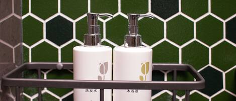 Two bottles of Country hotel amenities on a metal shelf against a green hexagonal tile wall.