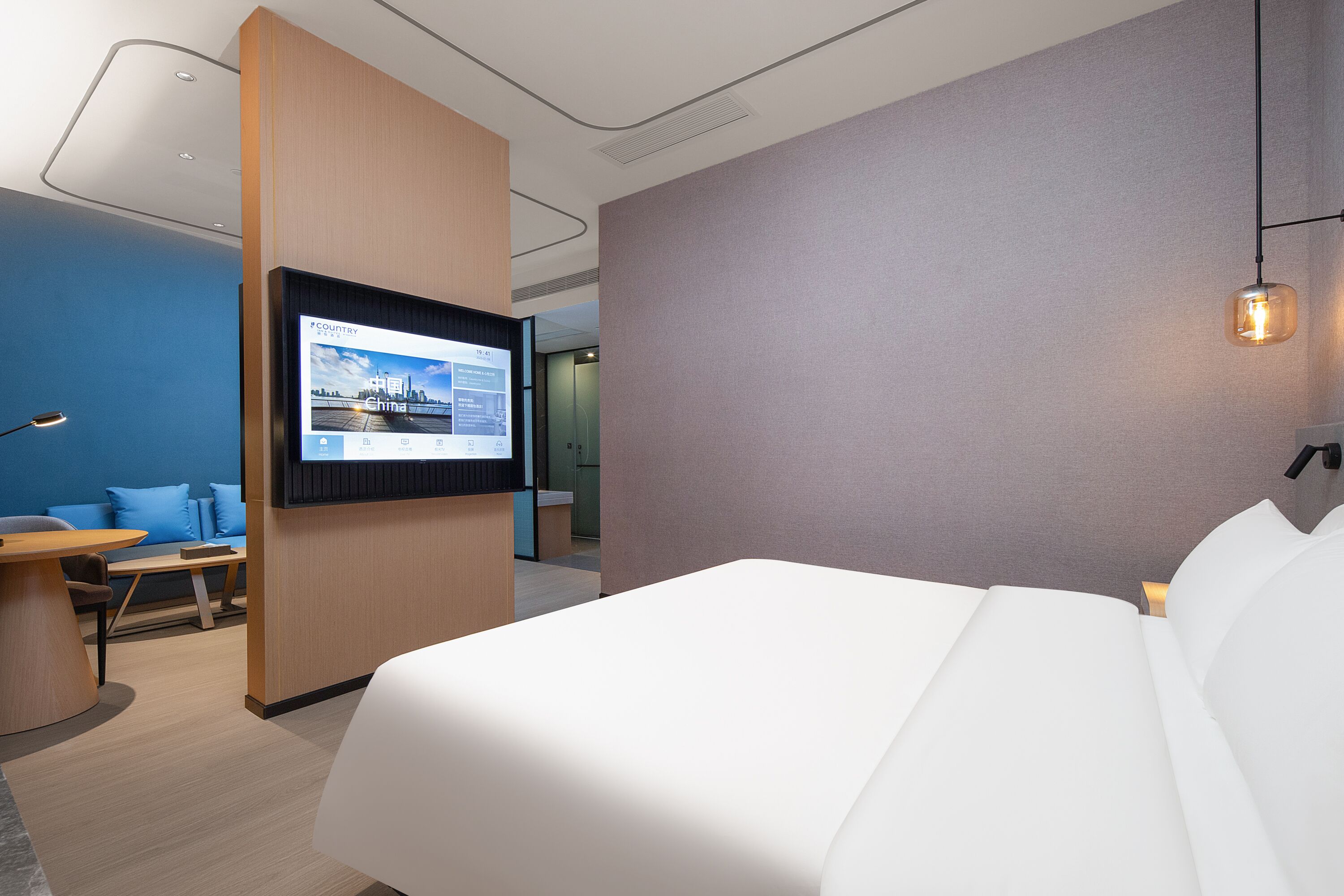 Ein modernes Hotelzimmer mit einem großen Bett, einem Schreibtisch und einem Fernseher, der eine Stadtansicht zeigt.