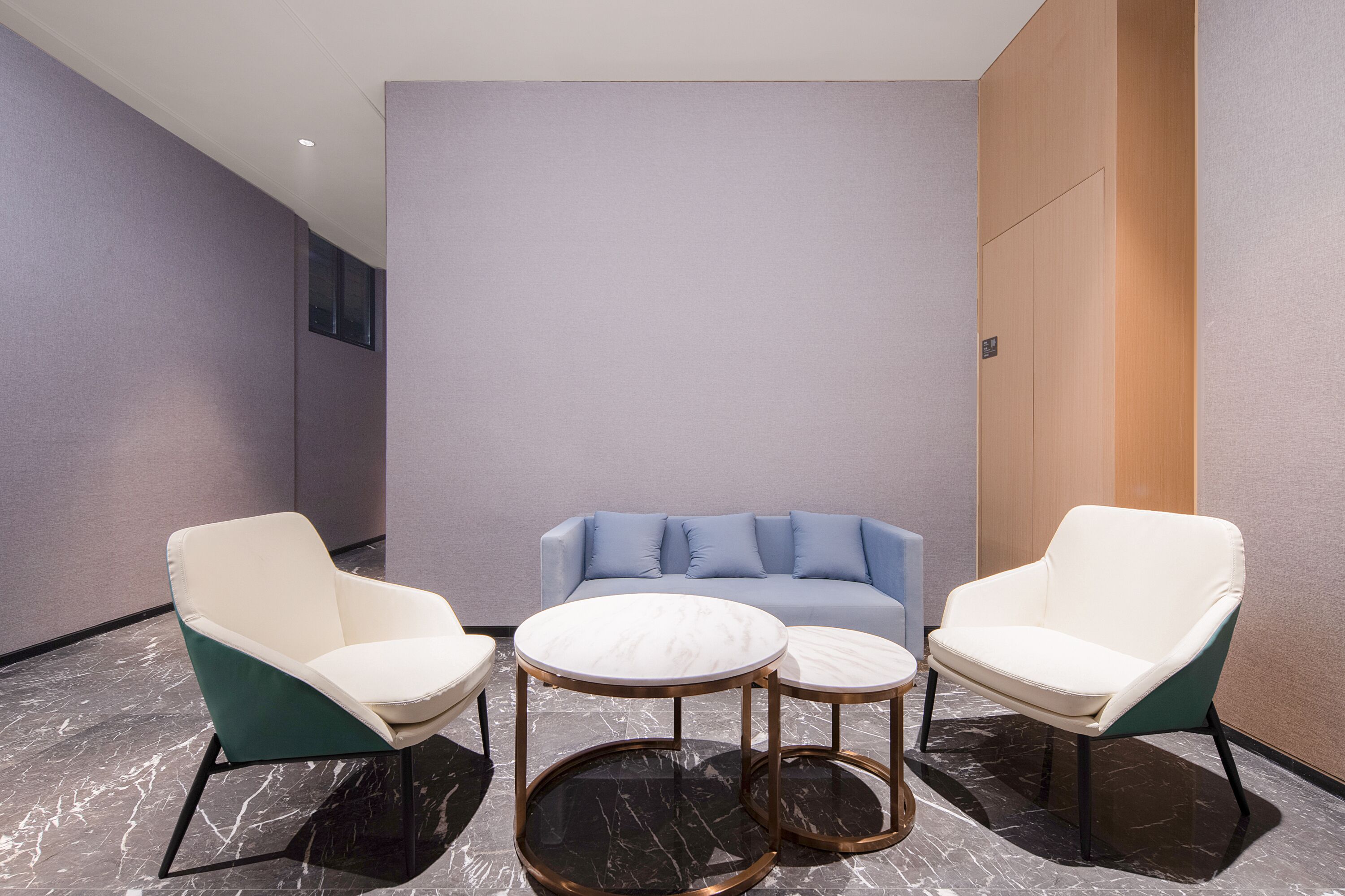 A modern lounge area with two white armchairs, a blue sofa, and two marble-topped coffee tables.