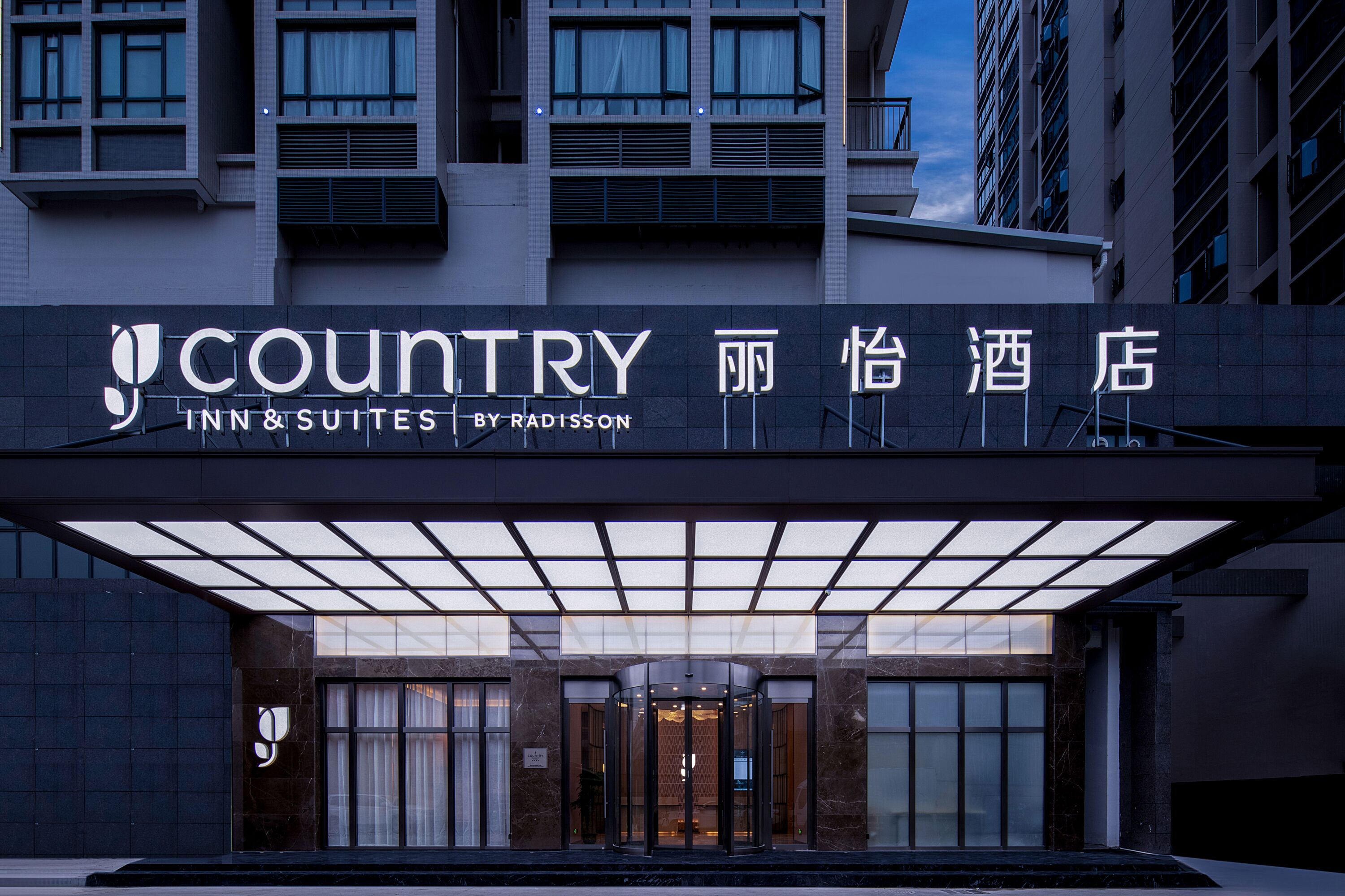 The exterior of a hotel with a modern design, featuring a prominent entrance with a revolving door and a sign indicating it is a country inn and suites by Radisson.