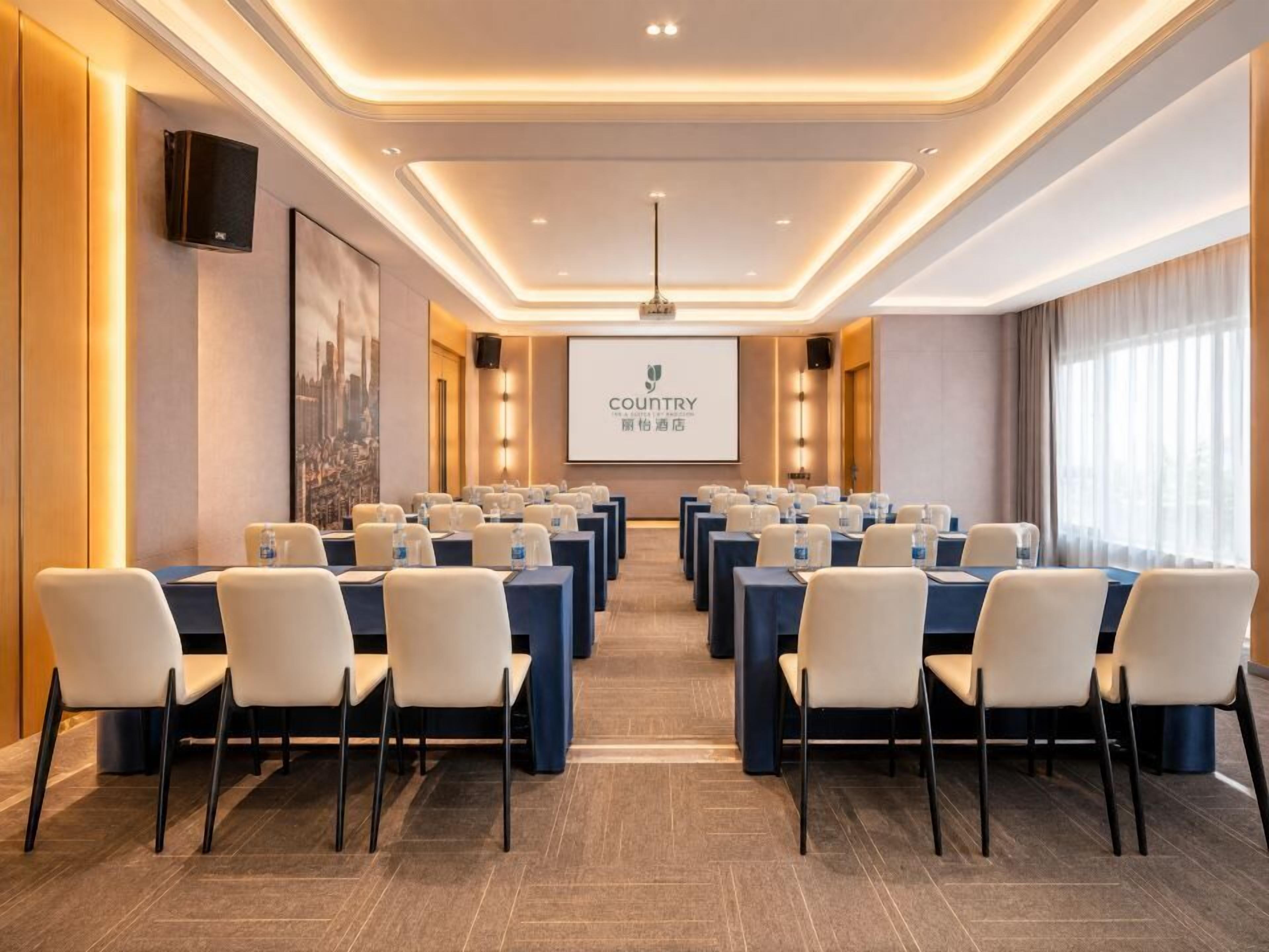 A conference room with rows of tables and chairs, a projector screen, and a large window.