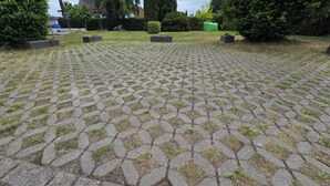 A paved courtyard with a geometric pattern, surrounded by greenery and a distant building. - Dachgeschosswohnung - Erholung mit Waldblick (Mustin)