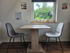 Un coin repas comprenant une table et deux chaises, une fenêtre donnant sur un paysage verdoyant et des œuvres d’art murales.