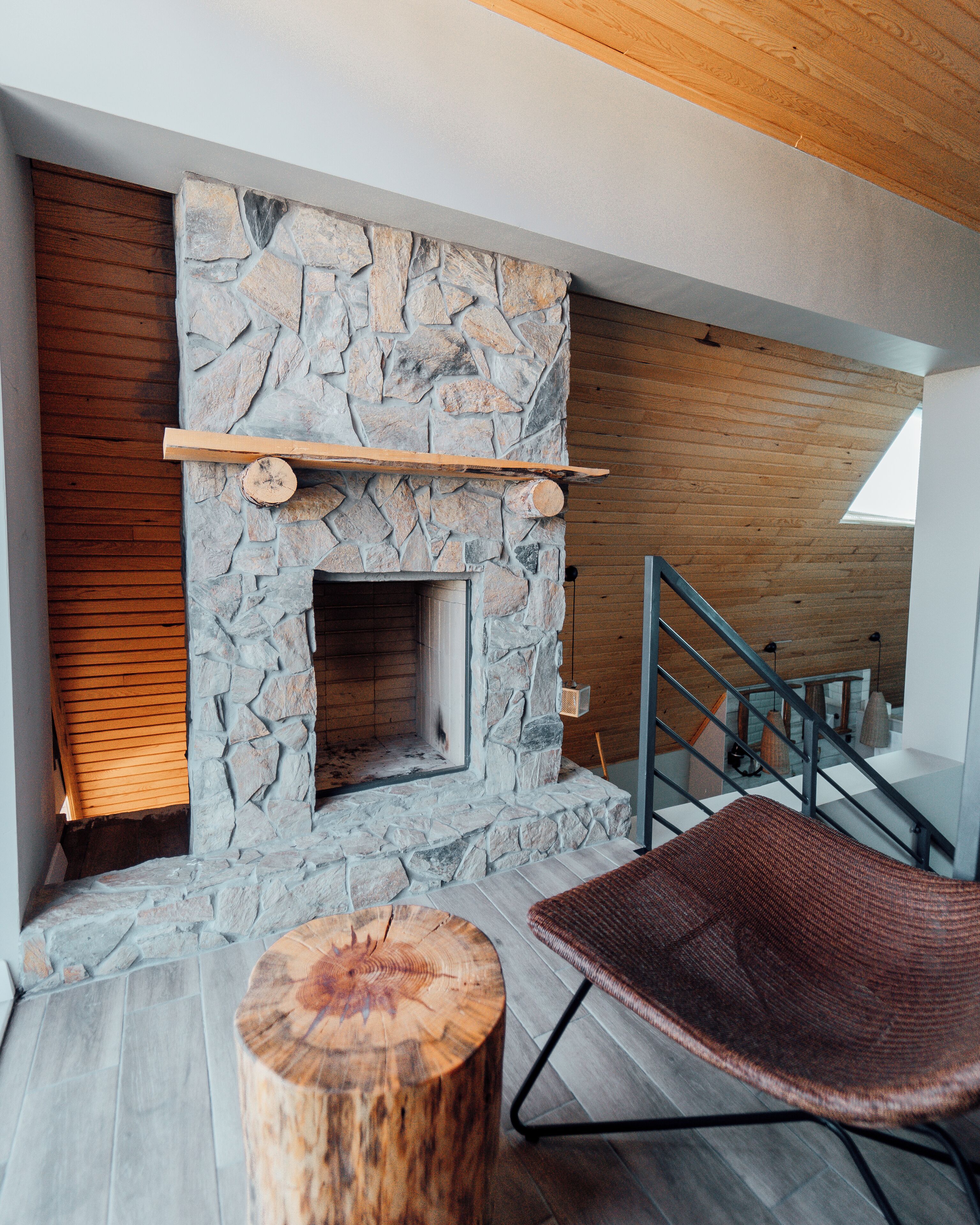 Un interior moderno con chimenea de piedra, listones de madera, una escalera y una silla de fibras naturales.