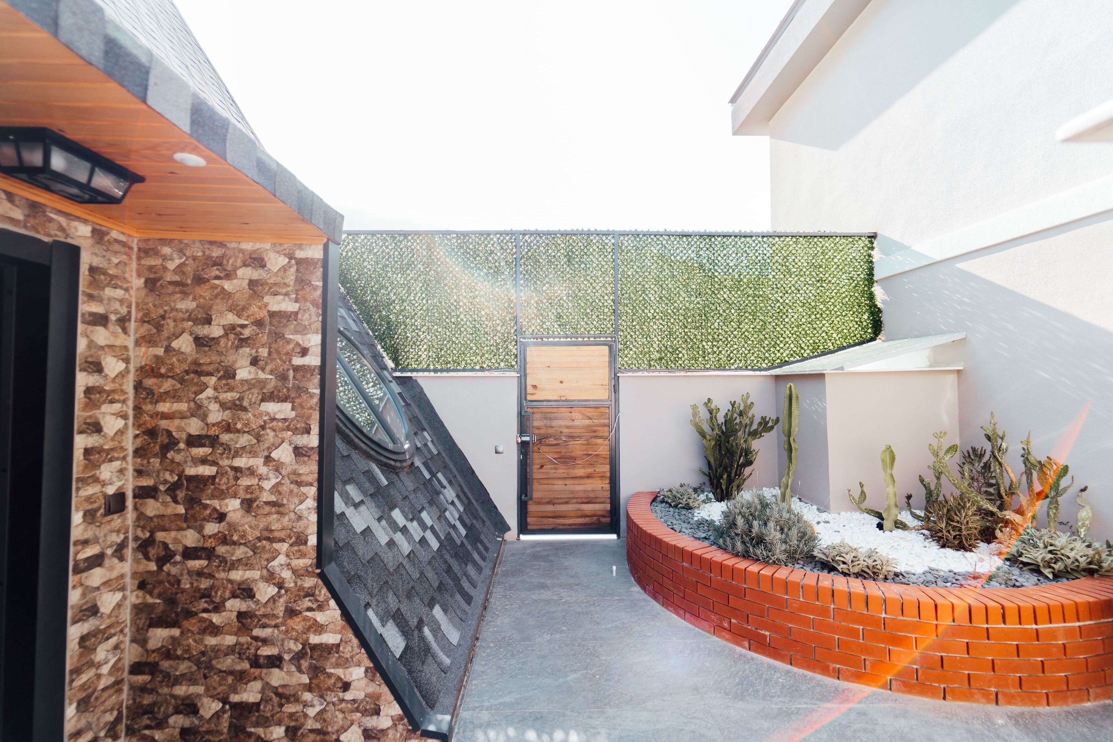 Un ambiente esterno moderno con un muro in pietra, una porta in legno e un fioriera in mattoni con cactus.