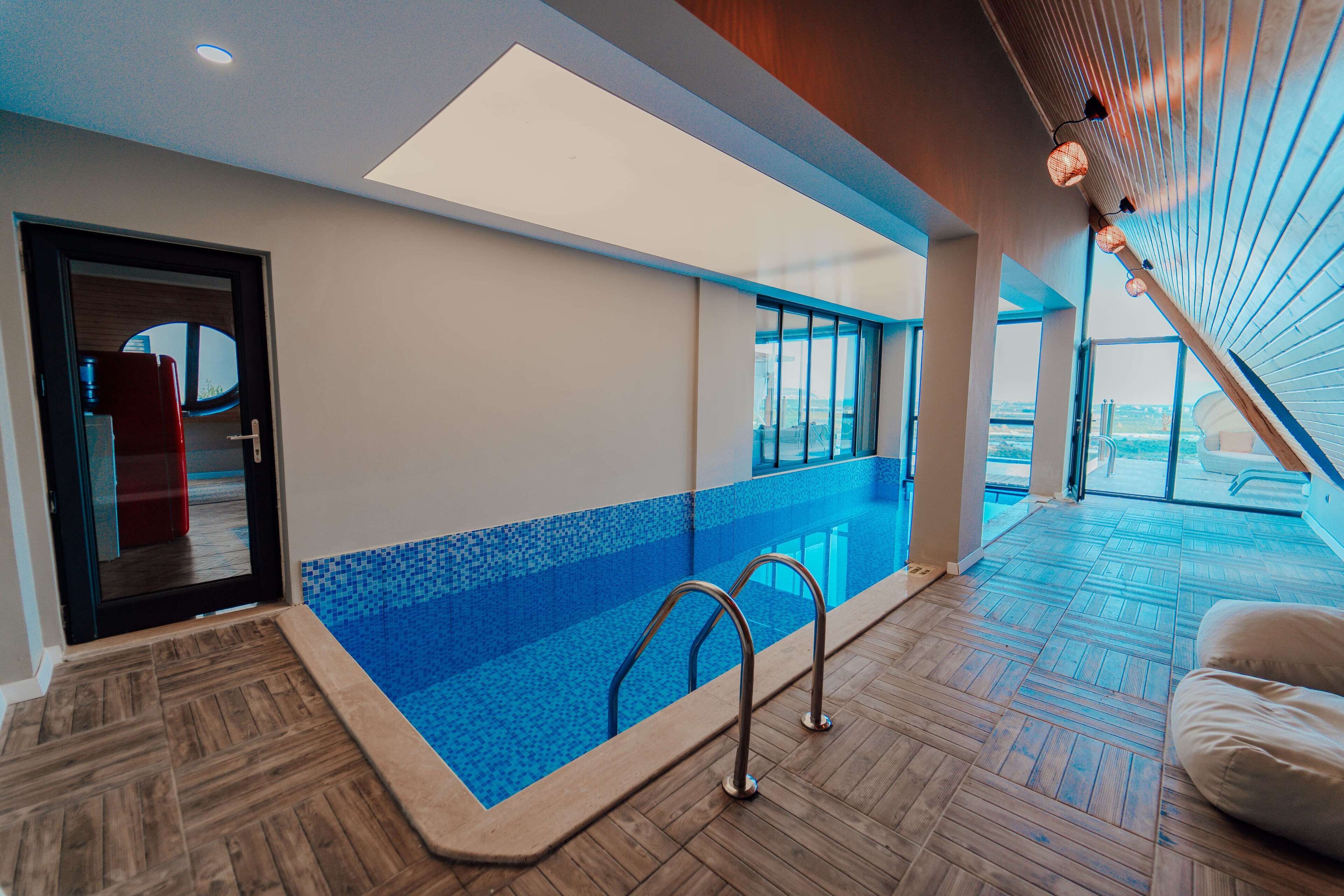 A modern indoor swimming pool with a wooden floor, a glass barrier, and a skylight.