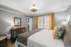 Una habitación de hotel con una cama grande, un escritorio, una silla y un ventanal con cortinas.