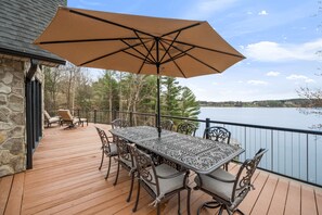 Una terraza de madera con una mesa, sillas y una sombrilla, con vista a un lago.