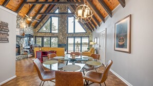 A dining area with a round glass table surrounded by brown chairs, a stone wall, and a wooden ceiling.