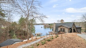 A lakeside cabin with a stone exterior, a deck, and a view of the lake.