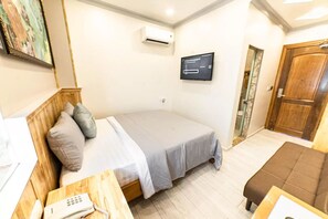A bedroom with a bed, a wooden nightstand with a phone, a TV on the wall, and a wooden door. - Thao Nho Hotel Phu Quoc - by Bay Luxury (Phu Quoc)