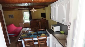 A compact kitchen with white cabinets, a microwave, and a sink. There is a dining table with chairs and a red couch in the adjacent living area. - Gite de Mon Clocher Appartement 3ième Étage Avec Balcon Proche du Mercantour (Roquebilliere)