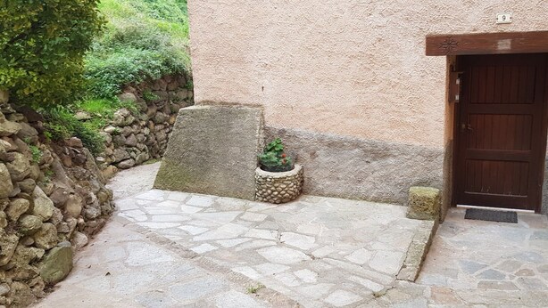A stone-paved courtyard with a rustic door and a small planter with a cactus. - Gite de Mon Clocher Appartement 3ième Étage Avec Balcon Proche du Mercantour (Roquebilliere)