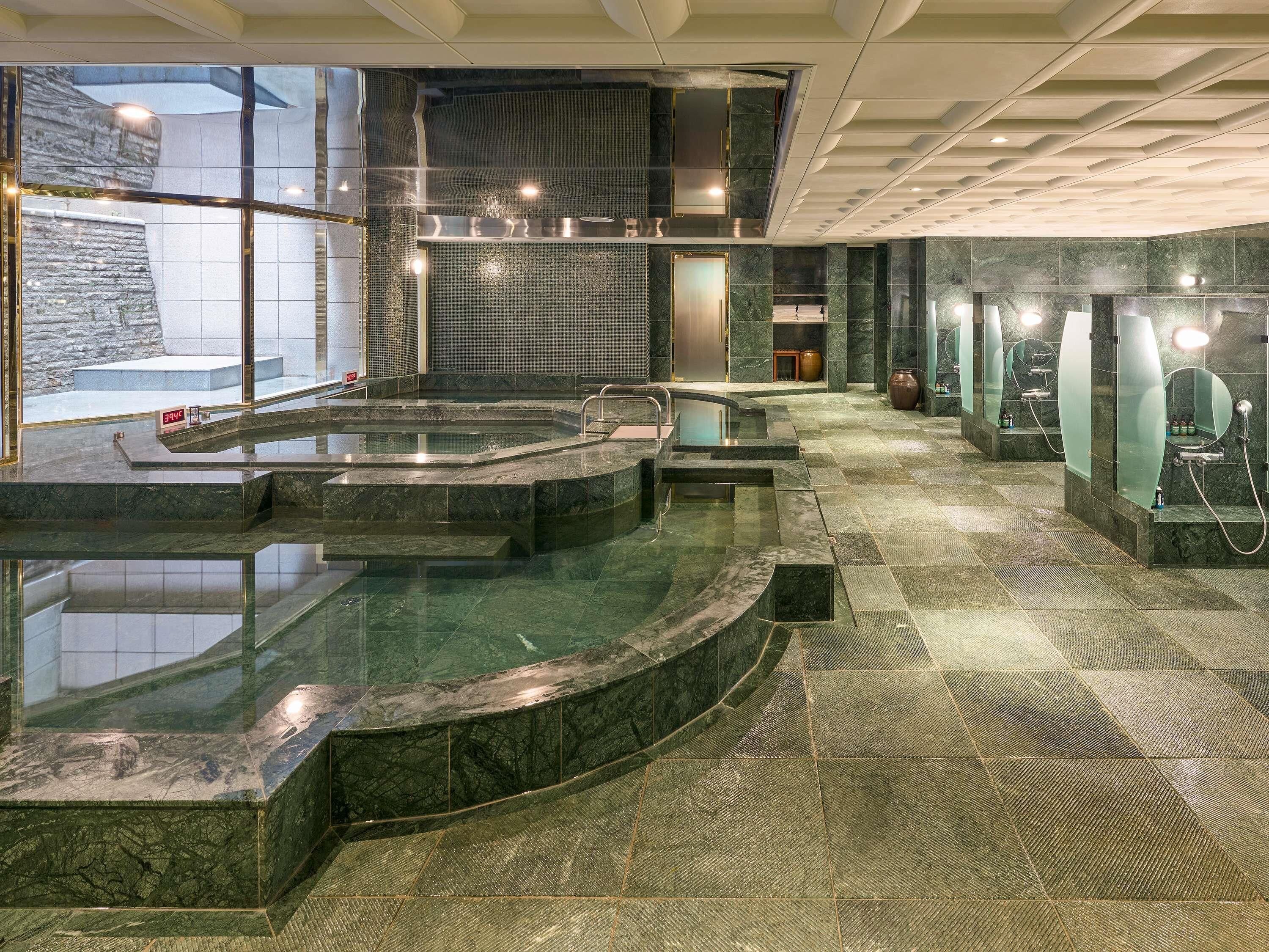 Uma área de piscina interior moderna com paredes de vidro, parede de pedra e chão ladrilhado.
