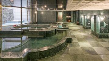 Uma área de piscina interior moderna com paredes de vidro, parede de pedra e chão ladrilhado.