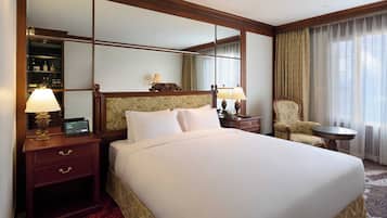 A hotel room with a large bed, a nightstand with a lamp, a chair, a small table, and a mirror.