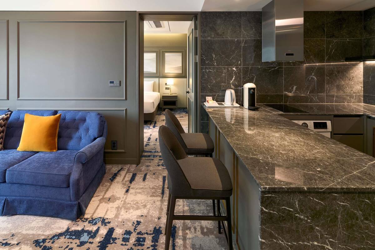 Quarto de hotel moderno com sofá azul, ilha de cozinha em mármore e uma área de quarto separada.