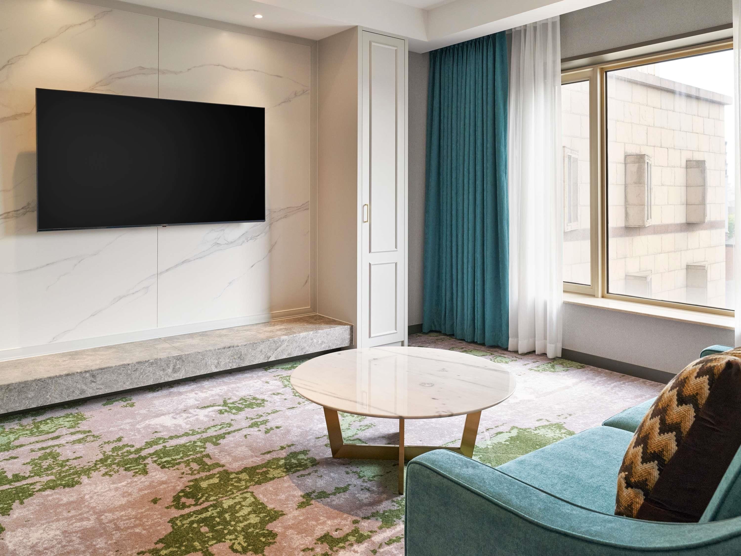 Una sala de estar moderna con un televisor de pantalla plana, un sofá, una mesa de centro y vistas a través de una ventana.